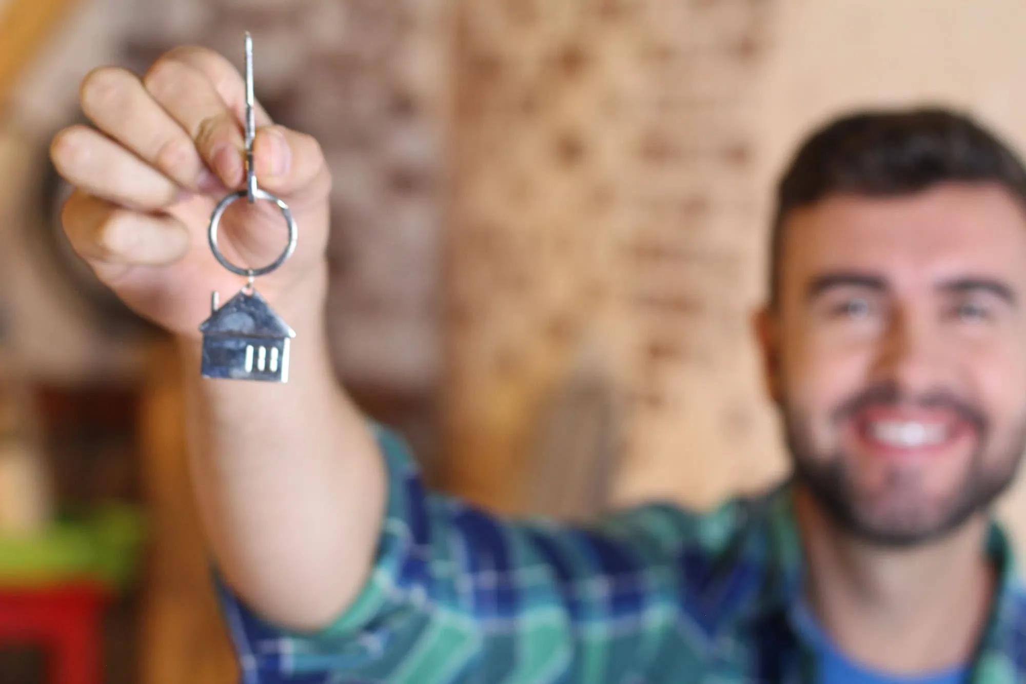 man holding a key with a house shaped keyring up to the camera due to AB 1556